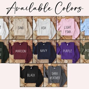 May include: A display of cropped sweatshirts in various colors, including white, sand, ash, light pink, and light blue. Other colors are forest green, maroon, navy, purple, military green, black, and dark heather. The text "Available Colors" is at the top.