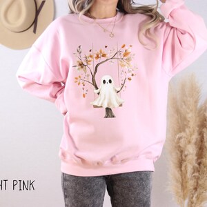 May include: Light pink sweatshirt featuring a whimsical illustration of a ghost on a swing beneath a tree with autumn leaves. The text "LIGHT PINK" is printed at the bottom. The sweatshirt is a comfortable, casual style.