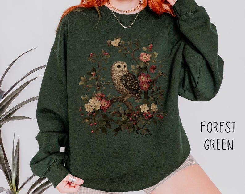 Op de afbeelding: Donkergroene sweatshirt met een uil en bloemenontwerp. De uil is bruin en wit, en de bloemen zijn roze en cr&egrave;me. De tekst "FOREST GREEN" staat rechtsonder. Comfortabele, casual stijl.