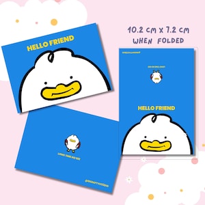 以下が含まれることがあります： 青いグリーティングカード、漫画のアヒルのデザイン。カードには「HELLO FRIEND」と「LONG TIME NO SEE」の文字が入っています。折りたたんだカードのサイズは10.2cm x 7.2cmです。カードは@RKRAFTYSTUDIOからです。
