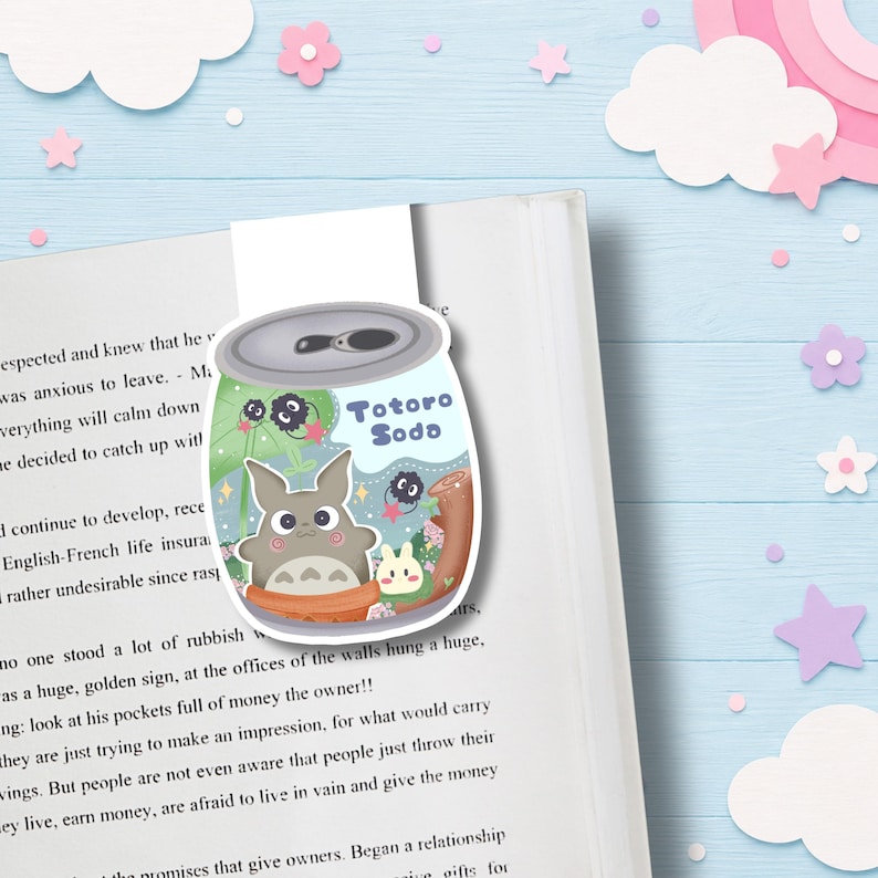 Op de afbeelding: Een magnetische boekenlegger in de vorm van een frisdrankblikje met een grijs wezen, een klein wit konijnachtig figuurtje en zwarte roetwezentjes. Het ontwerp bevat de tekst Totoro Soda in het blauw op een lichtgroene en blauwe achtergrond met sterren.