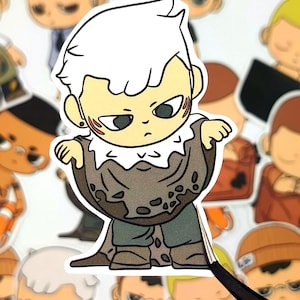 May include: A sticker featuring a cartoon character with white hair, wearing a brown cloak and green pants. The character has a stern expression and is surrounded by other similar stickers. The sticker is being held by a pair of tweezers.