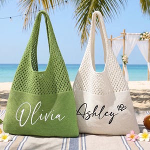 Pu&ograve; includere: Due borse tote a trama aperta, una verde e una bianco sporco, sono su una spiaggia. La borsa verde ha il nome "Olivia" in corsivo bianco, e la borsa bianco sporco ha "Ashley" con simboli di cuore. Le borse sono su una coperta a righe con fiori e frutta tropicali.