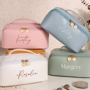 Puede incluir: Cuatro bolsas de maquillaje personalizadas en diferentes colores. Las bolsas están hechas de un material suave de piel sintética y tienen un cierre de cremallera. Las bolsas están etiquetadas con los nombres "Ashley", "Kathy", "Rosalie" y "Margery".