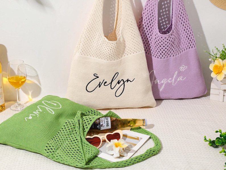 Pu&ograve; includere: Tre borse tote personalizzate in maglia color crema, lavanda e verde. La borsa color crema ha "Evelyn" in corsivo nero, la borsa lavanda ha "Angela" in corsivo bianco e la borsa verde ha "Olivia" in corsivo bianco. La borsa verde contiene occhiali da sole e una bottiglia.