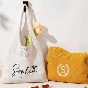 Pu&ograve; includere: Una borsa tote bianca a trama aperta con il nome "Sophia" in corsivo, accanto a una pochette gialla con una "S" bianca in una ghirlanda. Un cappello di paglia e fiori sono sullo sfondo.