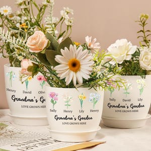 Puede incluir: Tres macetas de flores de cerámica blanca con un diseño floral y texto personalizado. El texto en las macetas dice "Grandma's Garden" e incluye nombres como "Henry", "David", "Lily" y "Sally".