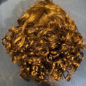 May include: A brown curly wig made of synthetic hair.