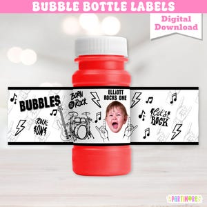 Könnte beinhalten: Eine rote Seifenblasenflasche mit weißem Deckel und umlaufendem Etikett. Das Etikett zeigt den Text "BUBBLES", "ROCK ON", "BORN TO ROCK" und "ELLIOTT ROCKS ONE". Das Design umfasst Noten, eine Gitarre, ein Schlagzeug und ein Babygesicht.