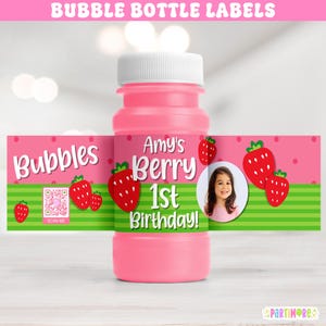 May include: Pink bubble bottle with a white cap and a label that reads "Amy's Berry 1st Birthday!" with strawberry graphics. The label also includes the word "Bubbles" and a QR code. The background is pink with green stripes.