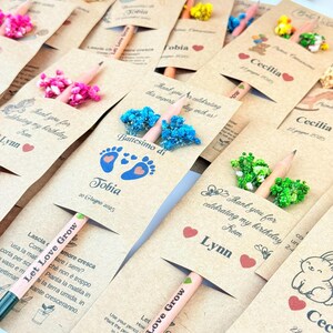 Puede incluir: Un conjunto de l&aacute;pices de semillas personalizados con adornos florales. Cada l&aacute;piz viene con una tarjeta con nombres, fechas y mensajes como "Thank you for celebrating my birthday". Los l&aacute;pices son de color rosa claro y tienen el texto "Let Love Grow."