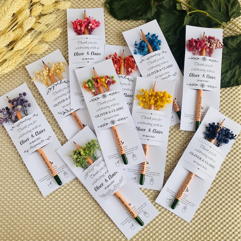 May include: A collection of personalized pencil favors with dried flowers. Each pencil is paired with a card that reads "Thank you for celebrating with us Oliver & Claire 20 April 2024". The pencils have green tips and the text "Love Grow".