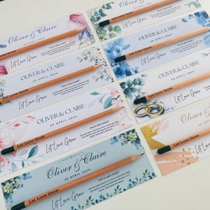 May include: A set of six wedding favor pencils with a watercolor floral design and the text "Let Love Grow". Each pencil has a black eraser and is packaged in a clear cellophane bag. The pencils are personalized with the couple's names and wedding date.