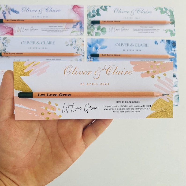 May include: A wedding invitation card with a gold and pink abstract design. The card features the text "Oliver & Claire" and "20 April 2024". A wooden pencil with the text "Let Love Grow" is included. The card also includes instructions on how to plant seeds using the pencil.