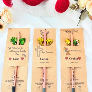 Puede incluir: Tres l&aacute;pices personalizados con sobres de semillas. Cada l&aacute;piz se muestra en una tarjeta de papel kraft con texto y elementos decorativos. Uno dice "Gracias por celebrar mi cumplea&ntilde;os de Lynn". Los otros dos dicen "Prima Comunione Cecilia 22 giugno 2025" y "Baby Shower Cecilia 22 giugno 2025."