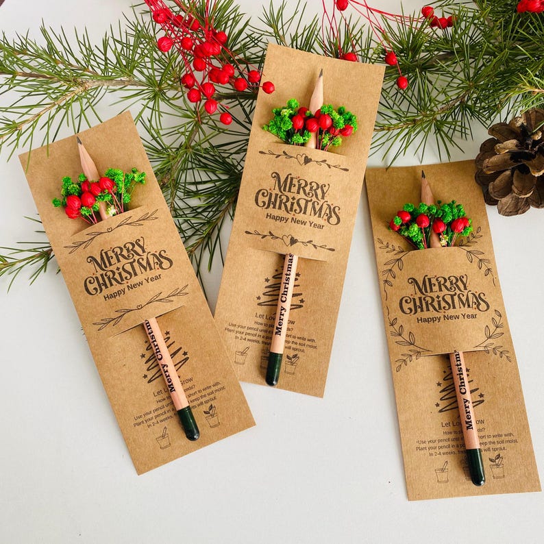 以下が含まれることがあります： クラフト紙のクリスマス鉛筆ギフトセット3つ。各セットには、「Merry Christmas」の文字が入った鉛筆、赤いベリーと緑の葉の小さなフラワーアレンジメント、「Merry Christmas Happy New Year」の文字が含まれています。