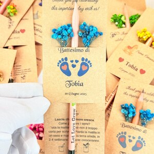Puede incluir: Recuerdos de papel kraft para un bautizo, cada uno con un l&aacute;piz, flores azules y el nombre "Tobia" y la fecha "20 Giugno 2025". Tambi&eacute;n se ve el texto "Thank you for celebrating this important day with us!"
