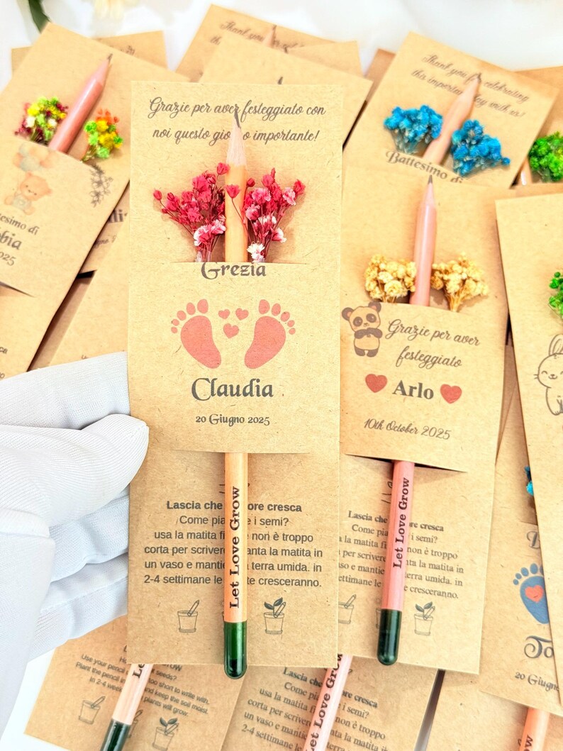 Puede incluir: L&aacute;pices de semillas personalizados con tarjetas. Las tarjetas color beige presentan texto e ilustraciones, incluyendo huellas de beb&eacute; y los nombres "Grezia" y "Arlo". Cada l&aacute;piz est&aacute; adornado con un peque&ntilde;o arreglo floral.