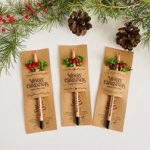 以下が含まれることがあります： 茶色のカードに、緑と赤い実で飾られた3本のクリスマス鉛筆。各カードには「MERRY CHRISTMAS Happy New Year」の文字が書かれています。お祝いのホリデーデコレーション。