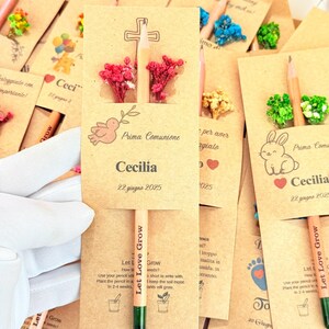 Puede incluir: Un conjunto de l&aacute;pices de semillas con tarjetas adjuntas. Las tarjetas son de color marr&oacute;n claro con varias ilustraciones, incluyendo una cruz, una paloma y un conejo. Los l&aacute;pices son de color naranja claro con puntas verdes y la frase "Let Love Grow".