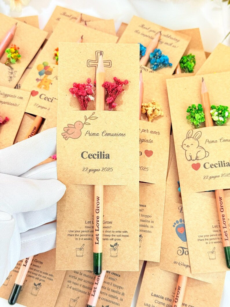 Puede incluir: Un conjunto de l&aacute;pices de semillas con tarjetas adjuntas. Las tarjetas son de color marr&oacute;n claro con varias ilustraciones, incluyendo una cruz, una paloma y un conejo. Los l&aacute;pices son de color naranja claro con puntas verdes y la frase "Let Love Grow".