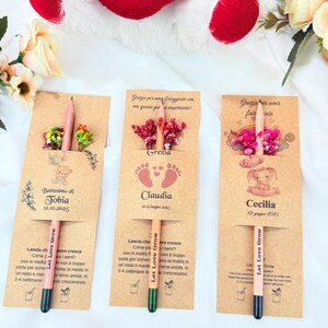 Puede incluir: Tres recuerdos de l&aacute;pices personalizados con detalles florales. Cada l&aacute;piz est&aacute; unido a una tarjeta con un nombre y una fecha, con el texto "Let Love Grow". Un peluche rojo en forma de coraz&oacute;n con "I Love You" est&aacute; en el fondo.