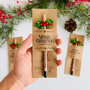 以下が含まれることがあります： クリスマスをテーマにした鉛筆ギフトセット。 鉛筆は「Merry Christmas Happy New Year」の文字が入った茶色のカードに入っています。 各鉛筆は、赤いベリーと緑の葉の小さなアレンジメントで飾られています。