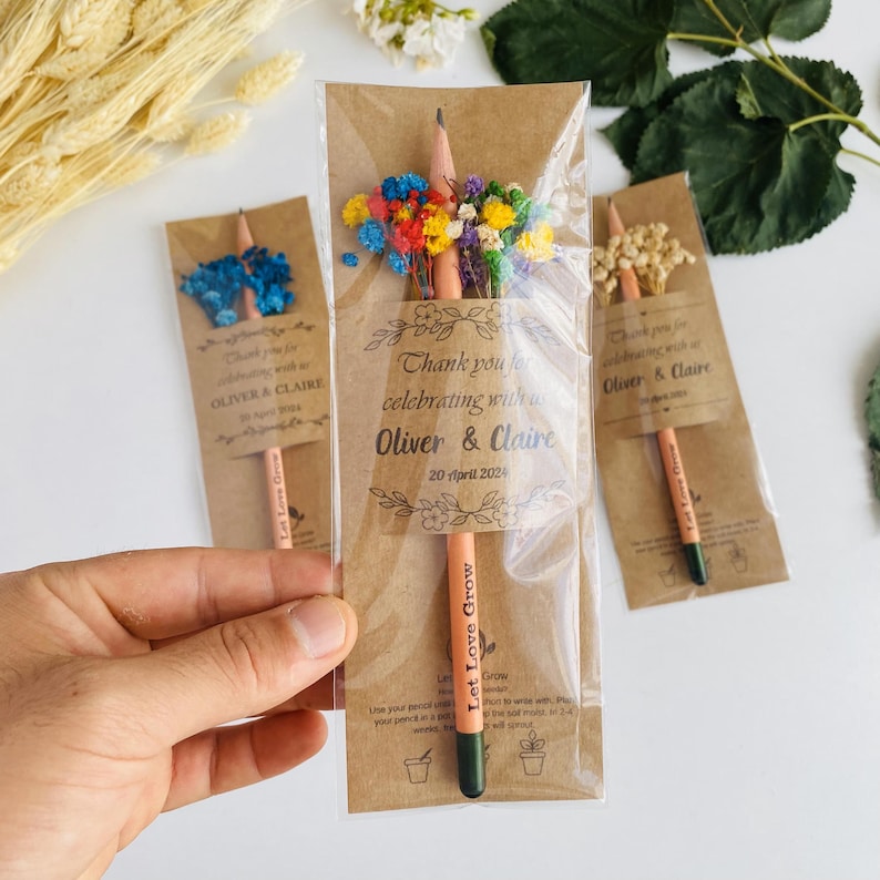 May include: Pencils with dried flowers, packaged in clear plastic with brown paper backing. The pencils have the text "Let Love Grow" and the paper says "Thank you for celebrating with Oliver & Claire, 20 April 2024".