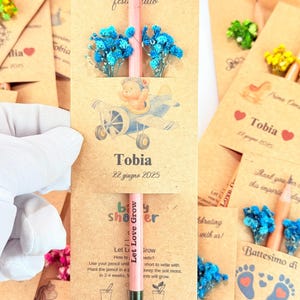 Puede incluir: Recuerdos de baby shower con l&aacute;pices rosas, flores secas azules y tarjetas. Las tarjetas presentan ilustraciones con temas de beb&eacute;s y el texto "Let Love Grow". Cada tarjeta est&aacute; personalizada con el nombre "Tobia".