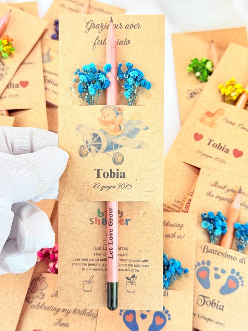 Puede incluir: Recuerdos de baby shower con l&aacute;pices rosas, flores secas azules y tarjetas. Las tarjetas presentan ilustraciones con temas de beb&eacute;s y el texto "Let Love Grow". Cada tarjeta est&aacute; personalizada con el nombre "Tobia".