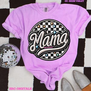 May include: A light purple t-shirt with a large, circular graphic that says "Mama" in a stylized font. The graphic has a black and white checkered background with star accents. The shirt is a comfortable, casual style.