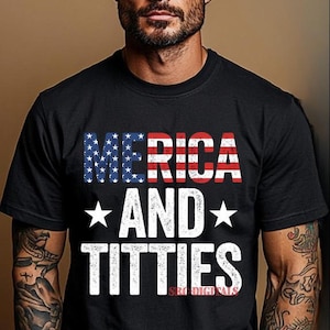 Peut inclure: T-shirt noir avec l'inscription blanche "'Merica AND TITTIES", le mot "'Merica" étant conçu dans le style du drapeau américain. Le t-shirt est porté par une personne avec des tatouages sur les bras.