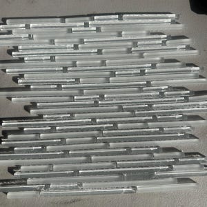 May include: A collection of rectangular, frosted glass tiles arranged in a staggered pattern. The tiles are a soft, translucent white, creating a subtle, textured surface. Ideal for backsplashes or accent walls.