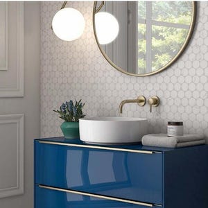 May include: A white bathroom vanity with a blue cabinet and a white porcelain sink. The sink has a gold faucet and a gold mirror above it. The wall behind the sink is tiled with small white hexagonal tiles.