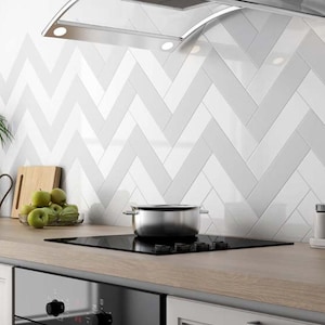 May include: A modern kitchen with a black cooktop, stainless steel pot, and white cabinets. The backsplash features a white and gray herringbone tile pattern. A stainless steel range hood is mounted above the cooktop. Green apples sit on the countertop.