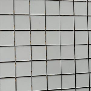 May include: Close-up of a grid of small, square, white tiles with dark grout lines. The tiles are arranged in a uniform pattern, creating a clean and modern aesthetic. Ideal for backsplashes or bathroom walls.