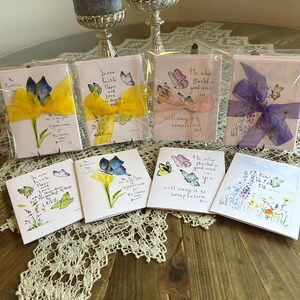 May include: Seven greeting cards with butterfly designs and inspirational quotes. The cards are decorated with ribbons and flowers. The quotes include "Now faith, hope, and love abide, these three; but the greatest of these is love." and "He who started a good work in you will carry it to completion."