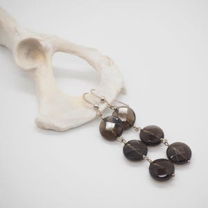 May include: A pair of silver earrings with three smoky quartz beads on each earring. The beads are round and faceted.