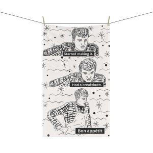 May include: A black and white kitchen towel with a repeating pattern of a man's face and the text "Started making it. Had a breakdown. Bon appétit."