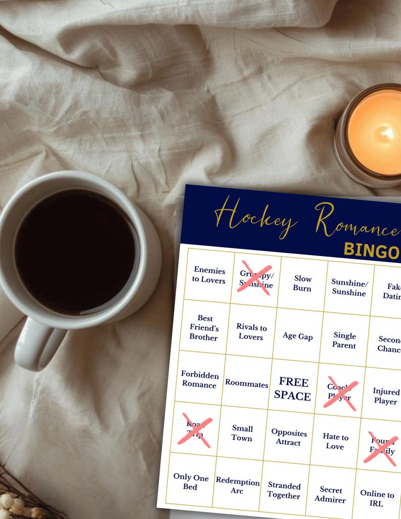 Puede incluir: Una tarjeta de juego "Hockey Romance Bingo" azul marino y blanca con una taza de caf&eacute; y una vela encendida. La tarjeta de bingo presenta tropos de novelas rom&aacute;nticas, con algunas casillas marcadas con una X.