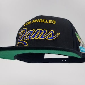 May include: Black and green baseball cap with the words "Los Angeles Rams" embroidered in yellow and blue.