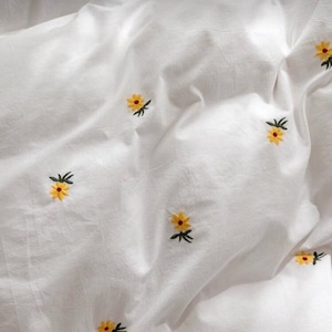 May include: White bedding with embroidered yellow and orange flowers. The flowers are scattered across the fabric, creating a delicate and cheerful pattern. The bedding appears to be made of a soft, lightweight material.