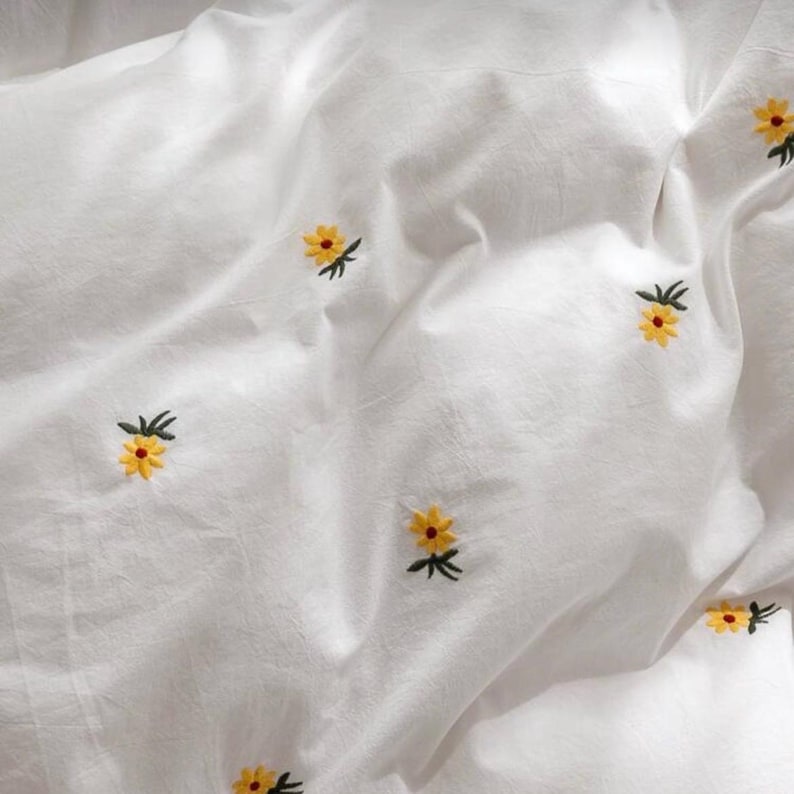 May include: White bedding with embroidered yellow and orange flowers. The flowers are scattered across the fabric, creating a delicate and cheerful pattern. The bedding appears to be made of a soft, lightweight material.