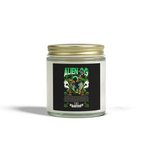 May include: A glass jar candle with a gold lid. The label features the text "ALIEN OG" in green and white, along with a graphic of an alien. The label also includes the text "18% HYBRID".