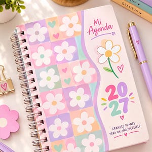 Può includere: Un'agenda 2027 a spirale intitolata Mi Agenda con un motivo a scacchi pastello decorato da fiori bianchi e piccoli cuori. La copertina riporta il testo Mi Agenda, 2027 e Grandes Planes Para Un Año Increíble con un'illustrazione floreale.