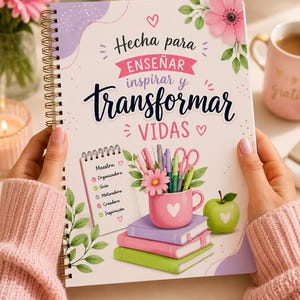 Puede incluir: Un cuaderno de espiral con el texto "Hecha para ENSEÑAR inspirar y transformar VIDAS" en una fuente decorativa. La portada presenta ilustraciones florales, una taza rosa con bolígrafos y una pila de libros. El cuaderno es sostenido por una persona que lleva un suéter rosa.