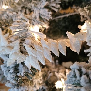 K&ouml;nnte beinhalten: Eine wei&szlig;e Muschel-Girlande, die an einem schneebedeckten k&uuml;nstlichen Weihnachtsbaum befestigt ist. Die Girlande besteht aus kleinen, wei&szlig;en Muscheln, die in einer Reihe angeordnet sind.