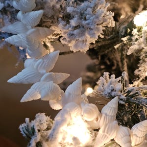 K&ouml;nnte beinhalten: Wei&szlig;e Muscheln, die als Girlande auf einem schneebedeckten k&uuml;nstlichen Weihnachtsbaum h&auml;ngen.
