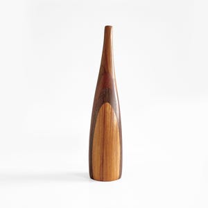 Puede incluir: Un jarrón de madera alto con un diseño delgado y curvado. El jarrón está hecho de múltiples tipos de madera, con una parte superior marrón oscuro, un centro marrón claro y una base de madera natural. El jarrón está sobre un fondo blanco.