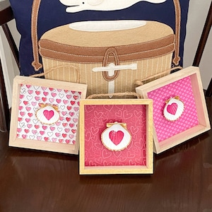 May include: Three framed decorative seashells with pink and white hearts on a pink background. The shells have a pink heart painted on the inside.